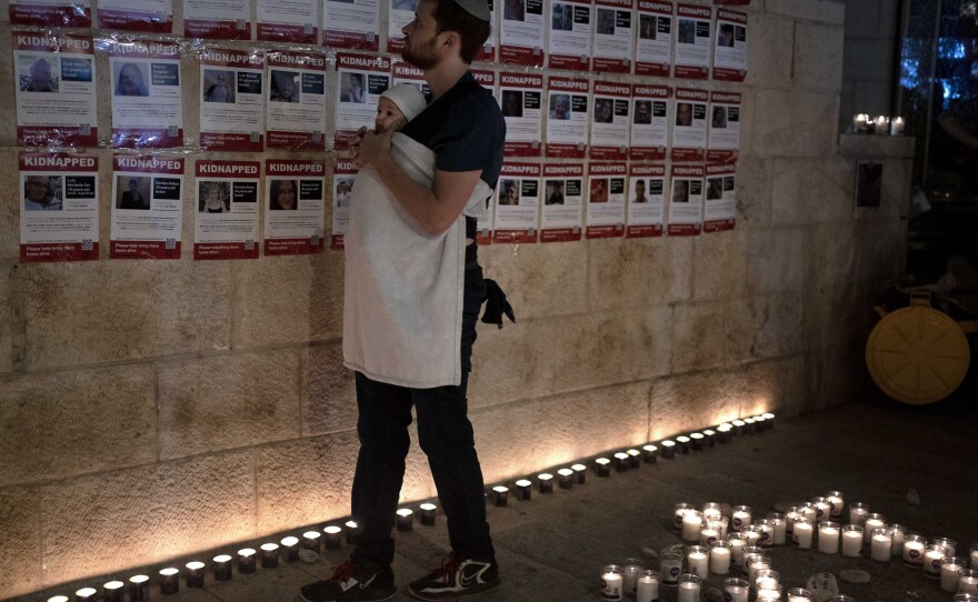 A man holds his baby as he looks at posters of the men, women and children held hostage by Hamas in the Gaza Strip, during a vigil marking 30 days since the Oct. 7 Hamas attack that started the fighting, in Jerusalem, Israel Sunday, Nov. 5, 2023.