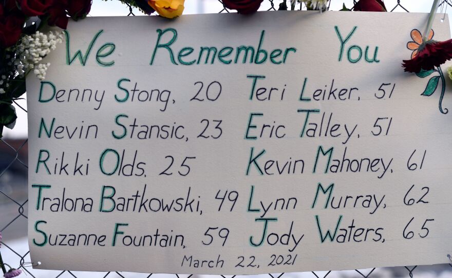 A sign framed with flowers lists the victims' names on the fence outside a King Soopers grocery store in Boulder, Colo. The suspected gunman is making his first court appearance on Thursday.