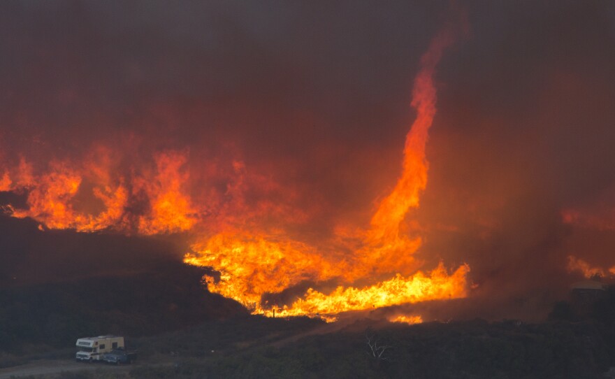 A fire tornado forms near cars parked on a country road at the Blue Cut Fire in 2016 near Wrightwood, California. Climate change is causing longer and more active fire seasons, according to the National Oceanic and Atmospheric Administration.