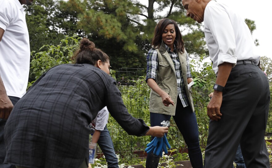 President Barack Obama is handed a pair of gardening gloves as first lady Michelle Obama, second from right, and NBA basketball player Alonzo Mourning, left, watch during the harvest of the White House Kitchen Garden on the South Lawn White House in Washington.