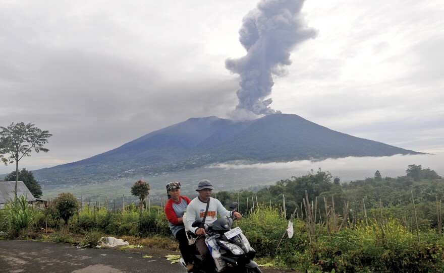 Motorists ride past by as Mount Marapi spews volcanic materials during its eruption in Agam, West Sumatra, Indonesia, Monday, Dec. 4, 2023.