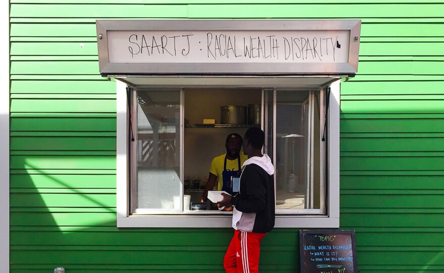 A customer approaches the window at Saartj, a pop-up food stall in New Orleans running a social experiment. Customers of color are charged the listed $12 price for a meal. White customers are told about the income gap in New Orleans between whites and African-Americans and asked if they want to pay $30 instead, a price that reflects the gap.