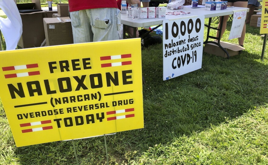 In this file photo, signs are displayed at a tent during a health event in Charleston, W.Va.  Public health officials say the spread of naloxone, also known as Narcan, has dramatically reduced overdose deaths in the U.S.