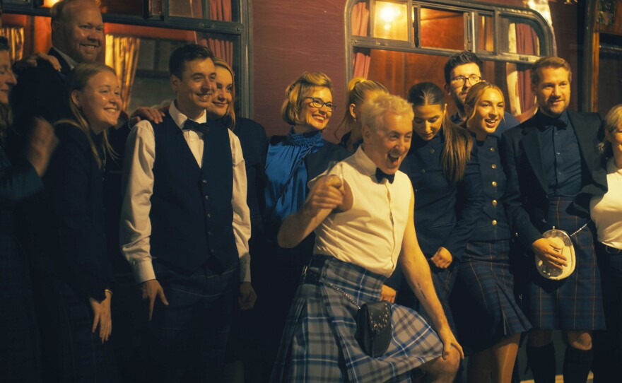 Alan Cumming wears a Scottish kilt and takes a photo with fellow passengers.