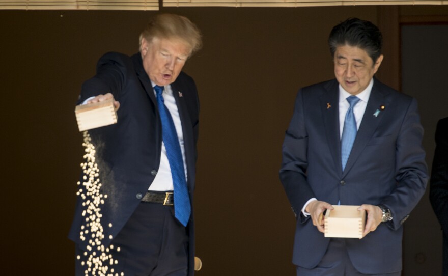 President Donald Trump pours the remainder of his fish food out as he and Japanese Prime Minister Shinzo Abe feed fish in a koi pond at the Akasaka Palace, on Monday.