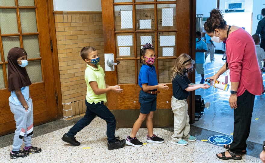 Quesada greets her second grade music class and gives them each a squirt of hand sanitizer as they enter her classroom.