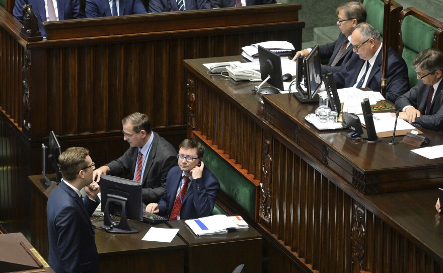Polish lawmakers voted overwhelmingly to remove prison penalties in a controversial Holocaust law. Prime Minister Mateusz Morawiecki (upper left) looks on as a right-wing lawmaker blocks the podium in a failed effort to obstruct the vote.