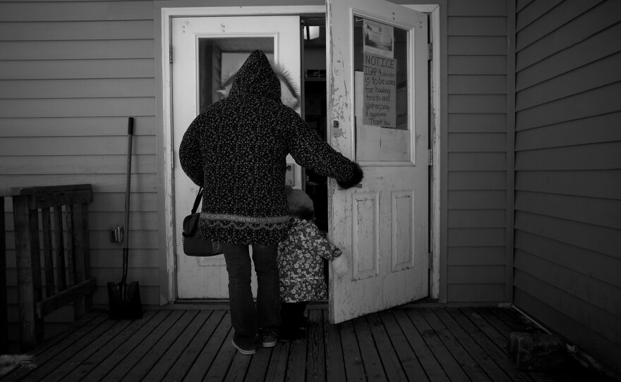 A woman holds the door for her daughter at the entrance to the Wales community center, where a meeting for local veterans turned into a gathering for many of the villagers in the tiny town.