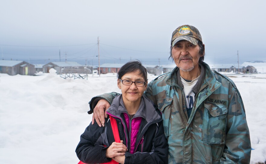 Sandra Gologergen and Wilfred Miklahook stand with the community of Savoonga, Alaska, in the background. Despite what appears to be lots of snow, Savoonga residents have been struggling with warmer-than-usual temperatures, which has led to challenging conditions for subsistence hunting.