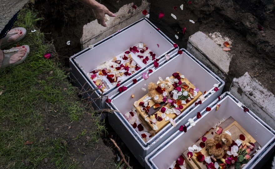 Attendees at the Garden of Innocence funeral drop rose pedals onto the coffins of an abandoned child inside its grave, San Diego, June 17, 2023.<br/>