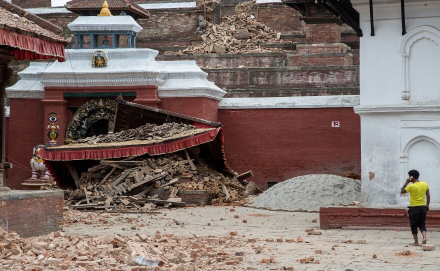 A young man speaks on the phone in front of a collapsed temple in the city center following an earthquake on April 25, 2015 in Kathmandu, Nepal. A strong magnitude-7.8 earthquake shook Nepal's capital and the densely populated Kathmandu Valley before noon Saturday, causing extensive damage.