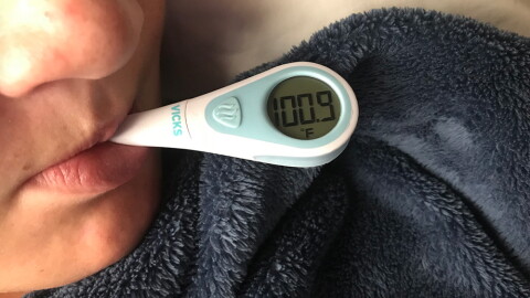 A boy with the flu takes his temperature at his home in San Diego, Feb. 14, 2018.
