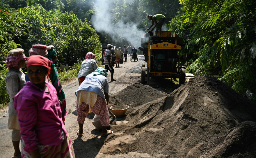 In a photograph from March 26, 2026, construction workers operating a tarmac mixer to build a road cutting through the island's forest land.