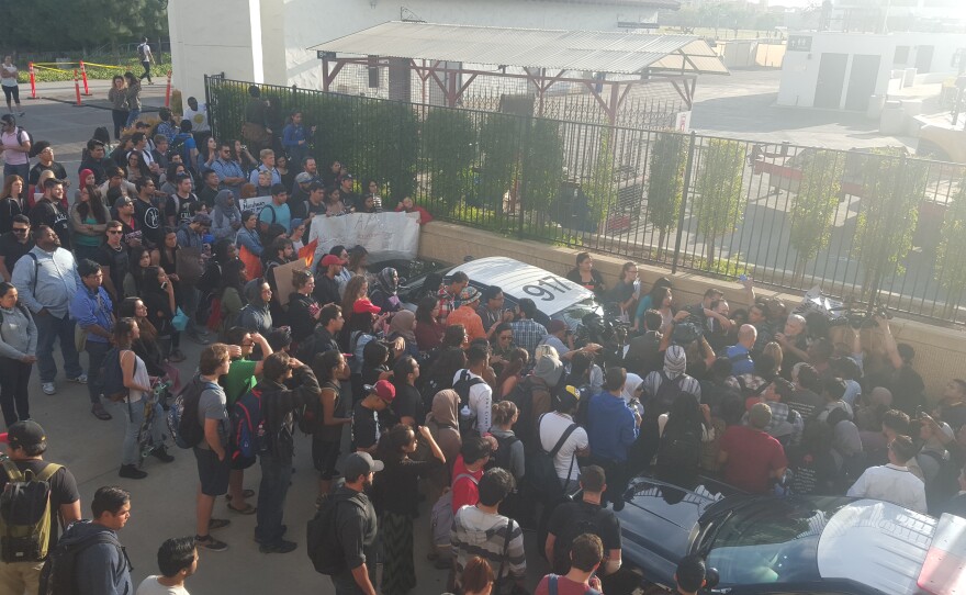 A crowd of protesters and members of the media surround a police car where San Diego State University President Elliot Hirshman was in, April 27, 2016.