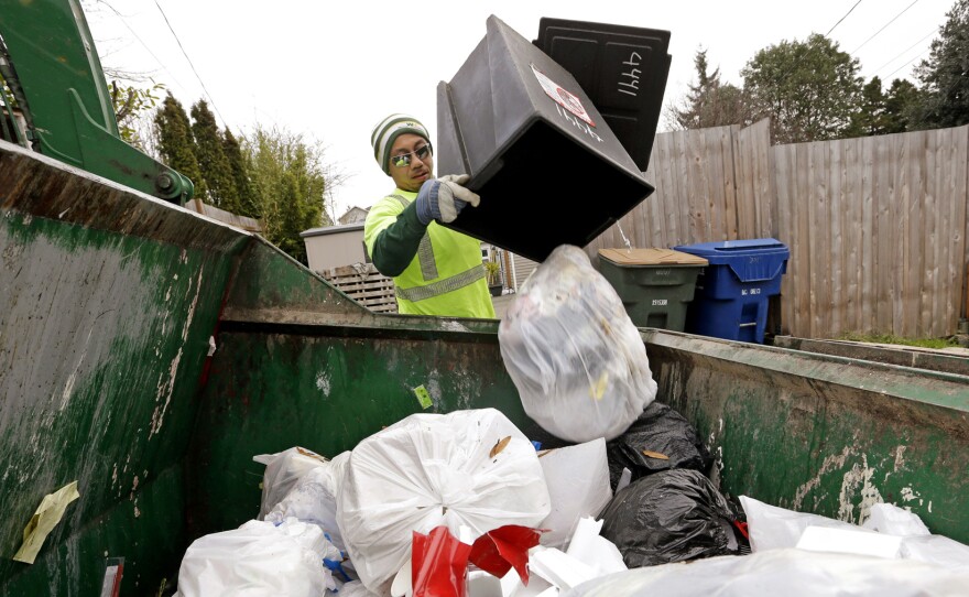 Seattle garbage collector Anousone Sadettanh empties a small residential garbage bin into his truck in 2014. It is now illegal to toss out food with the trash in the city. Residents will get warning tags for now; the city will start imposing fines in July.