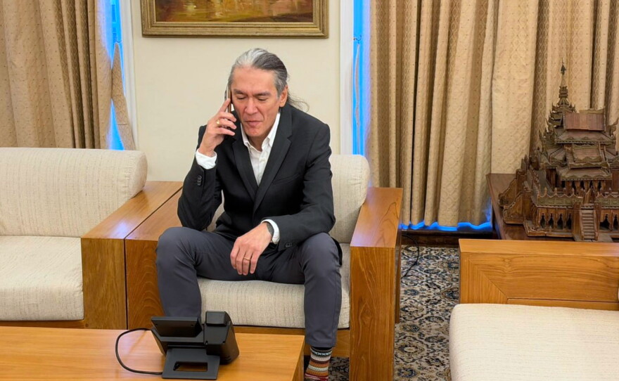 In this photo released by Myanmar's government on Thursday, Kim Aris, son of Myanmar's ousted leader Aung San Suu Kyi, talks on phone with his mother, at the Myanmar Embassy in London.