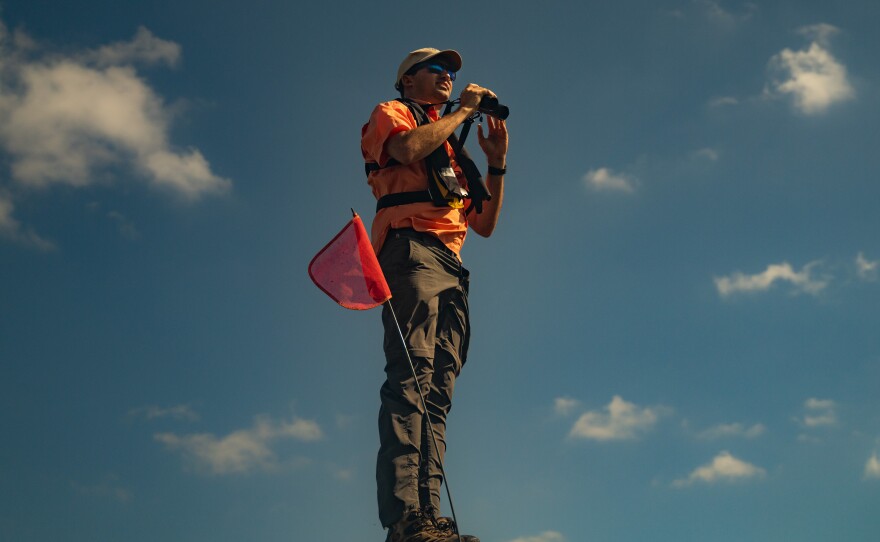 FWC Snail Kite Conservation Coordinator Tyler Beck stands on top of an airboat with binoculars to observe a Snail Kite at Lake Okeechobee in Moore Haven, Fla.