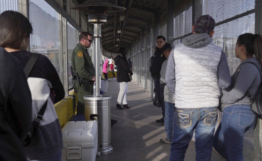 A Border Patrol agent and a U.S. Customs and Border Protection agent oversee the people waiting to cross into the U.S. from Matamoros, Mexico, at the Port of Entry in Brownsville, Tex., Tuesday, last month.