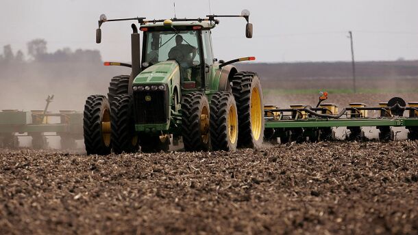 A green tractor that's planting corn moves across a brown dirt field in 2007 near Rochelle, Ill.