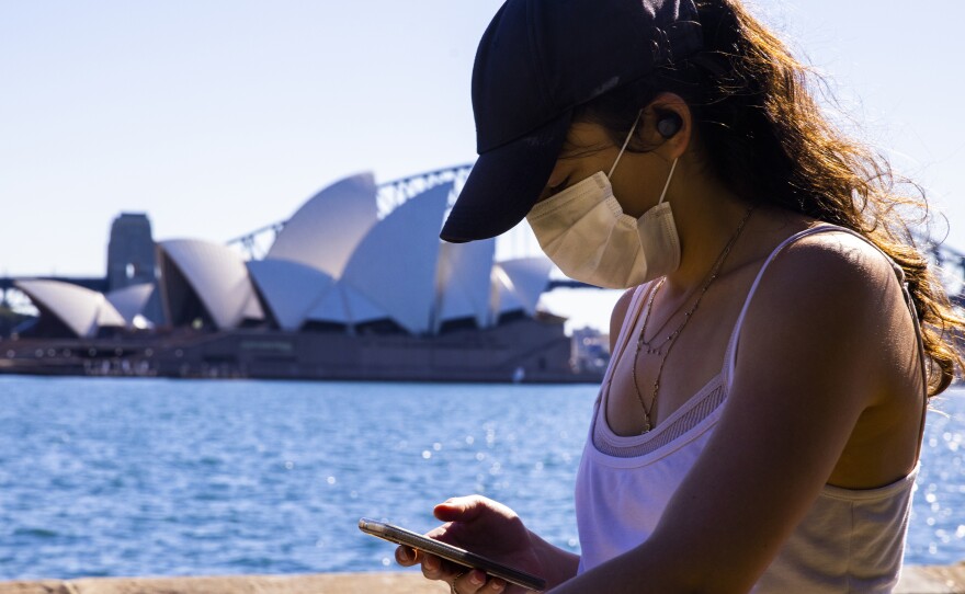 A woman looks at her phone outside the The Royal Botanic Gardens in Sydney, Australia on Aug. 6. The Indicator from Planet Money spoke to an economist for advice on how to cut back on digital dependency.