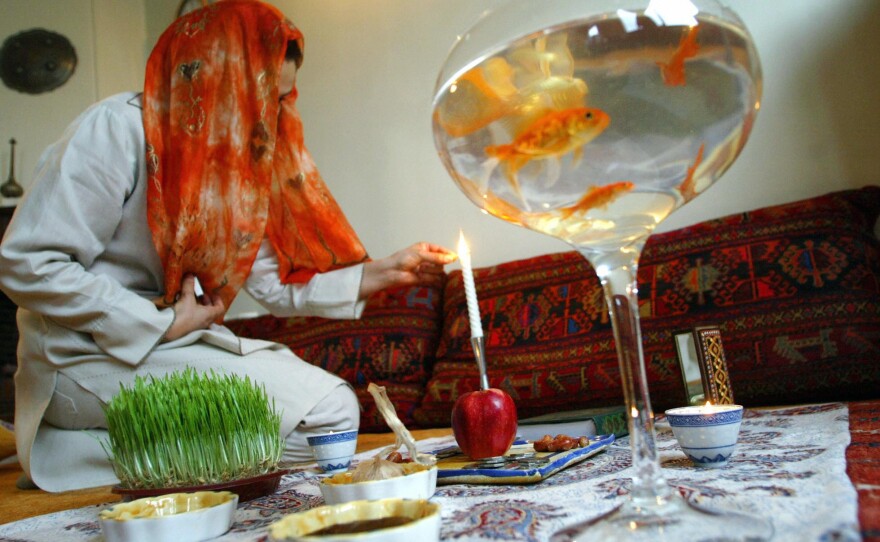 An Iranian woman in Tehran lights a candle on the ceremonial Nowruz table on the first day of the Iranian new year, March 2004. Some families add goldfish to the table to represent life.