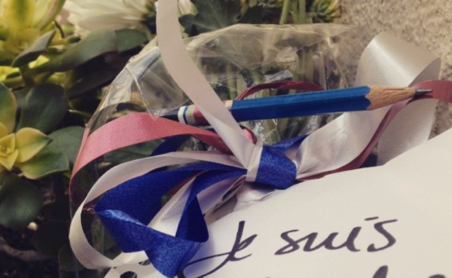 A bouquet of flowers is shown lying outside Balboa Park's House of France with a note stating "Je Suis Charlie."