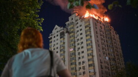 A woman looks at an apartment building burning after a Russian missile attack in Kyiv, Ukraine, Thursday, July 2, 2026. (AP Photo/Danylo Antoniuk)