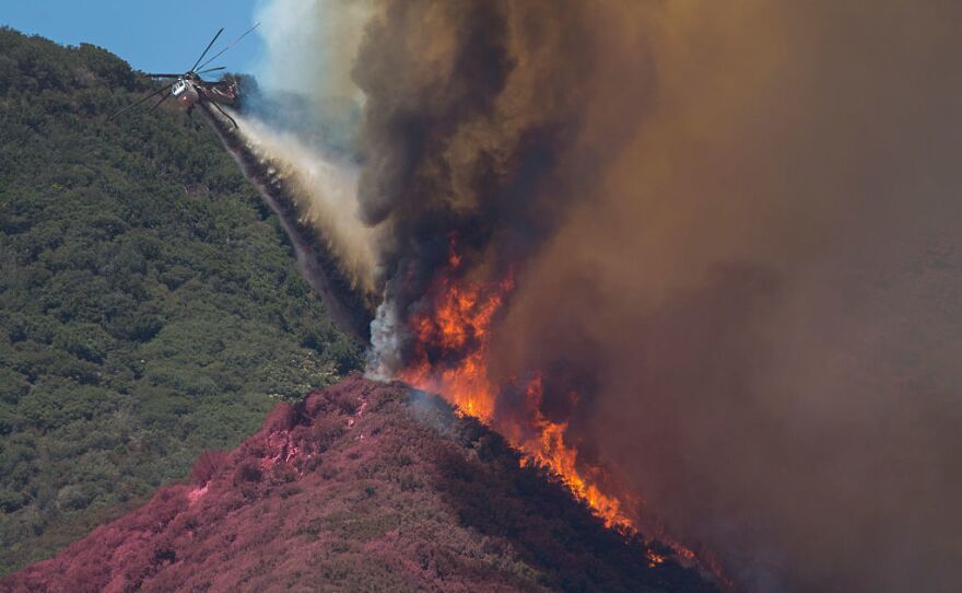 A firefighting helicopter pilot tries to stop flames close to jumping a ridge above Cajon Boulevard at the Blue Cut Fire on Thursday near Wrightwood, California.