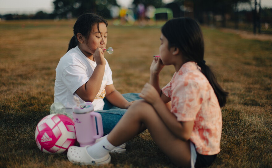 Cousins Kavya Saru, 9, and Denisha Saru, 8, blow bubbles as their sisters play soccer in Harrisburg, Pa., on Sept. 15, 2025.