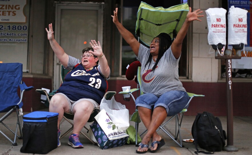 Misty Swegle (left) and Charlesetta Hawkins wave at passing motorists during rush hour on Tuesday in downtown Cleveland from their spot along the parade route for the city's celebration of the Cavaliers.