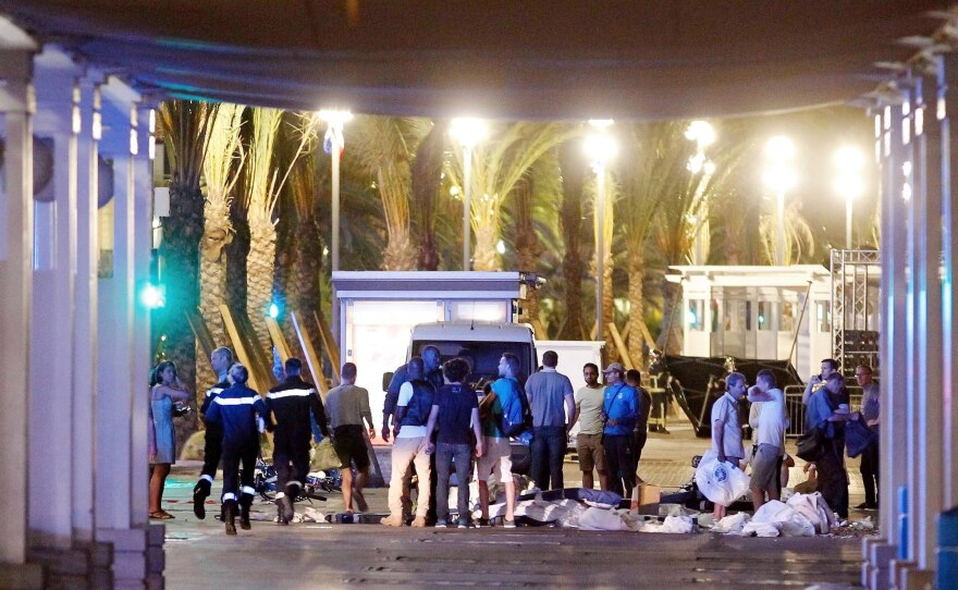 People stand next to covered bodies in the early hours of Friday on the Promenade des Anglais in Nice, southern France.