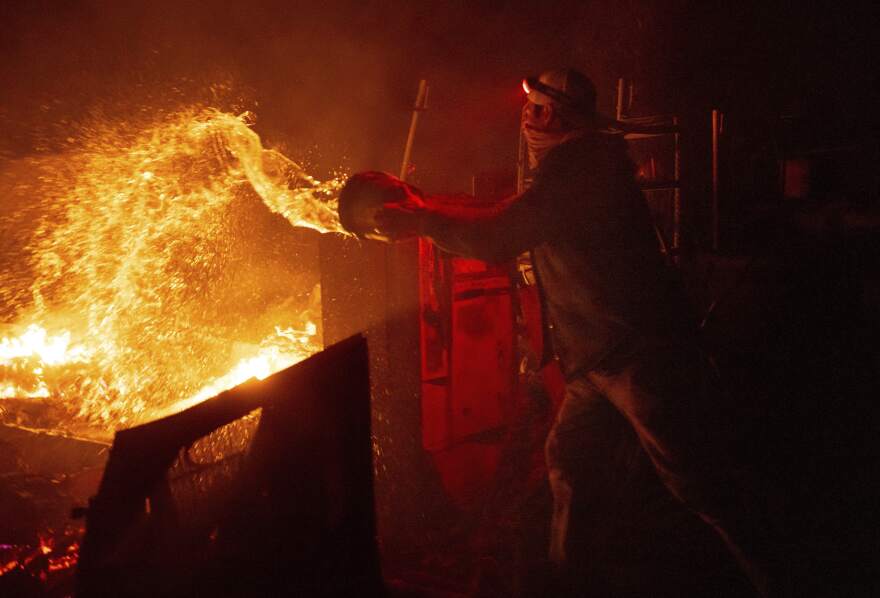 Francis Lopez douses flames with a bucket of water as a wildfire called the Highland Fire burns through his property in Aguanga, Calif., Monday, Oct. 30, 2023. A wildfire fueled by gusty Santa Ana winds ripped through rural land southeast of Los Angeles on Monday, forcing thousands of people from their homes, fire authorities said.