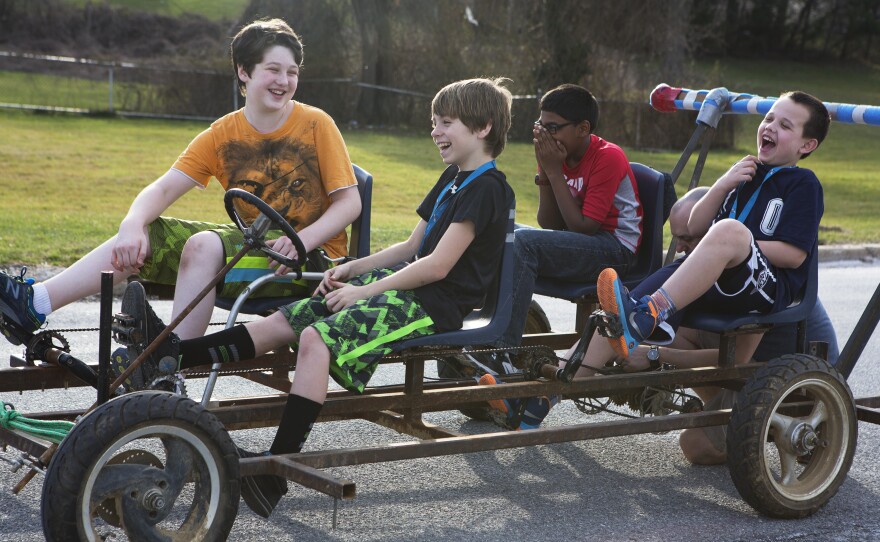 Sean Davis (left), Stephen Geisler, Rithik Kavanakudy and Andy Patterson laugh as they test drive the cart that will power their kinetic sculpture. Each year they reuse the cart's frame, which includes classroom chairs and bike chains, and create a new sculpture to go on top.