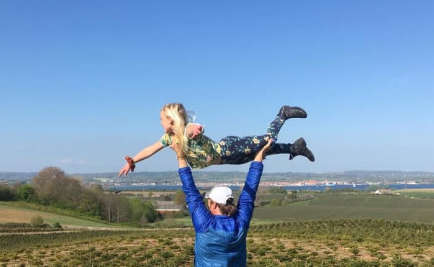 John lifts his young daughter above his head so she looks like she's flying above the horizon.