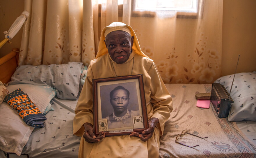 Sister Rosemary Luyiga, who's 95, holds a portrait of her late mother in the room where she lives within the residential compound.