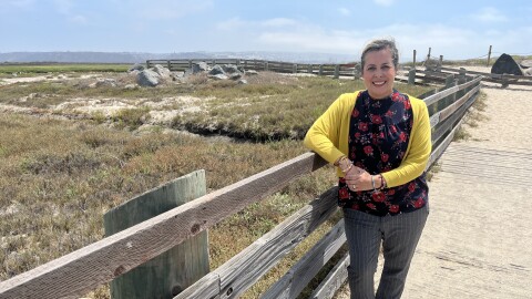 Playwright Mabelle Reynoso leans against a wooden fence at the Tijuana River Estuary, Aug. 20, 2025.