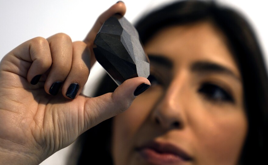 An employee of Sotheby's Dubai presents a 555.55 Carat Black Diamond called "The Enigma" on Monday that will be auctioned at Sotheby's Dubai gallery, in Dubai, United Arab Emirates.