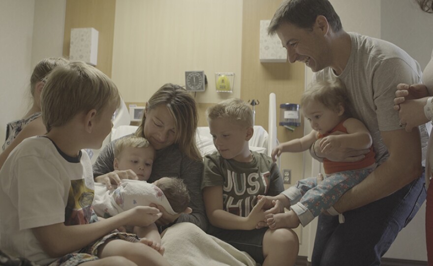 Cindy (center) is surrounded by her children after giving birth to a baby for intended parent Julian (standing right).