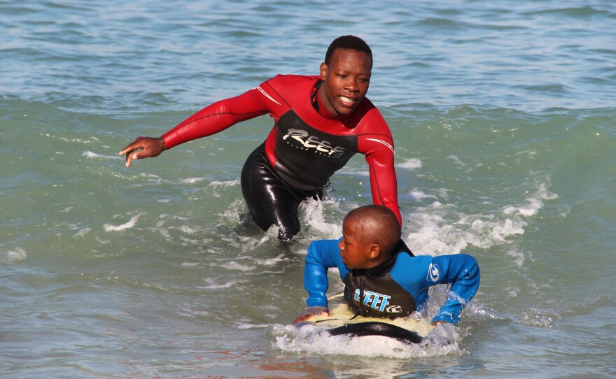 Lwandile Mntanywa helps a younger surfer learn to catch a wave. He's a "junior leader" in the Waves for Change program.