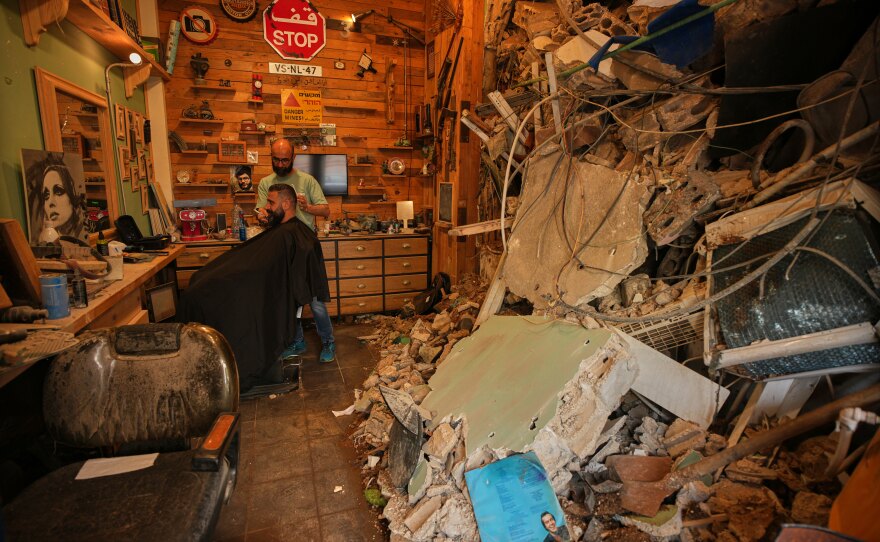 Barber Mohammad Mehdi cuts the hair of his client Ayman Al Zein inside his shop, which was damaged in an Israeli airstrike that also damaged Al Zein's shop, in Dahiyeh, Beirut's southern suburbs, Lebanon, Saturday, April 18, 2026.