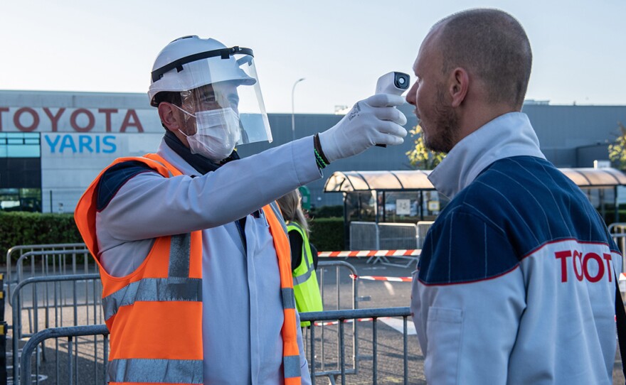A worker wearing protective gear checks an automobile assembly line worker's temperature at the entrance to a Toyota plant in Onnaing, France, on April 21. U.S. auto plants are preparing to reopen with new coronavirus safety protocols.