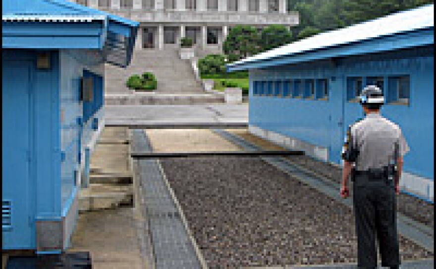 A South Korean soldier in the Joint Security Area in Panmunjom. The concrete strip at the end of the gravel at center marks the border. In the background is a North Korean building.