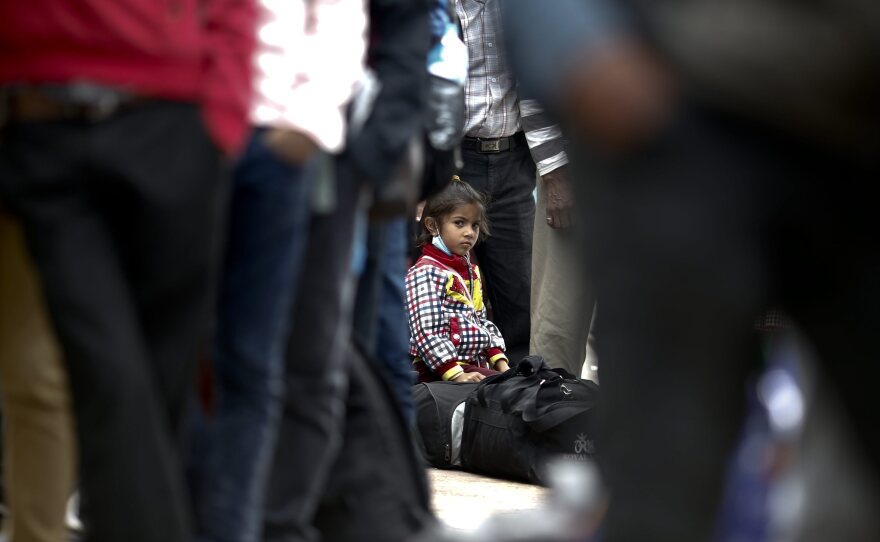 A young girl sits on her luggage as she waits in a long line with her family, hoping to board buses provided by the government to return to their homes outside Kathmandu.