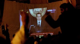 Protesters watch Egyptian President Hosni Mubarek give a speech on a projected television screen in Tahrir Square February 1, 2011 in Cairo, Egypt.