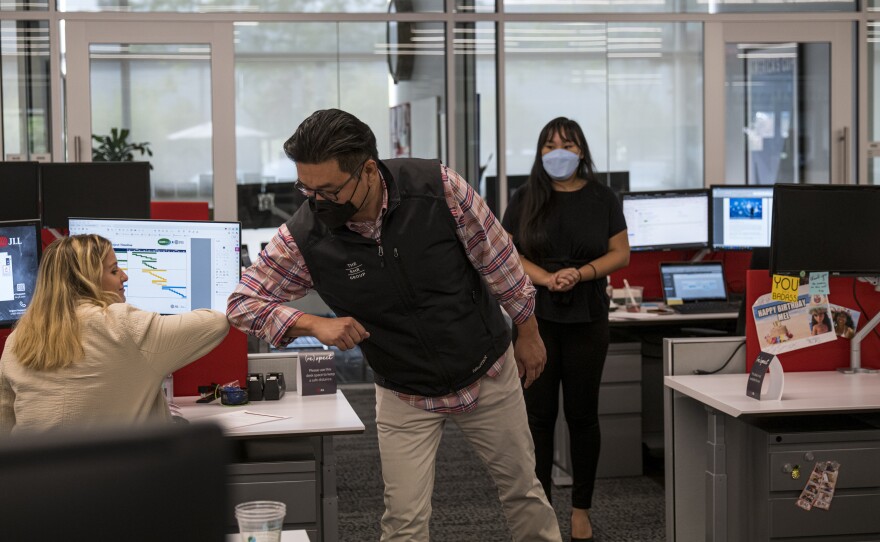 Employees elbow bump at a JLL office in Menlo Park, Calif., in September. With the delta variant surging, mask mandates are returning, and some employers are now requiring employees to be vaccinated before coming to the office.