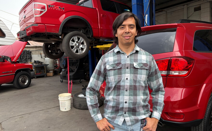 Guadalupe Higuera stands in front of trucks being repaired at his family's shop in Phoenix.