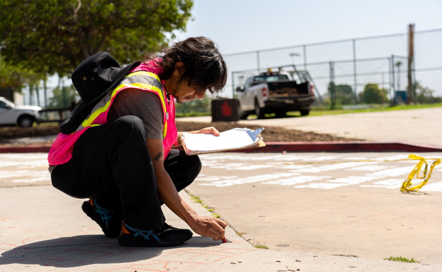 A project worker chalks the letters of a poem onto the pavement of a City Heights alley, marking where the words should be laid, on Tuesday, June 18, 2024.