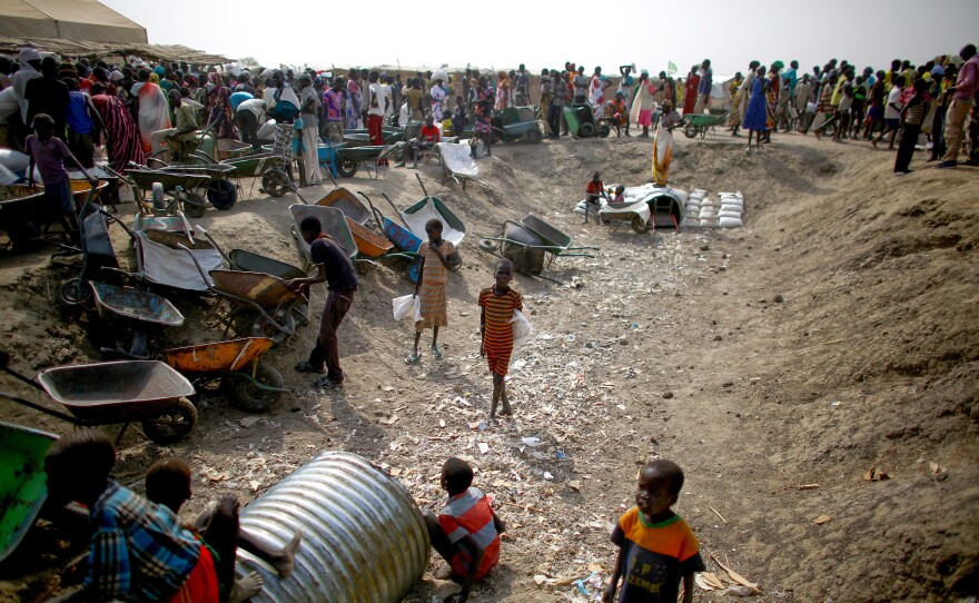 People stand in line for food rations while children play in a ditch at the camp.