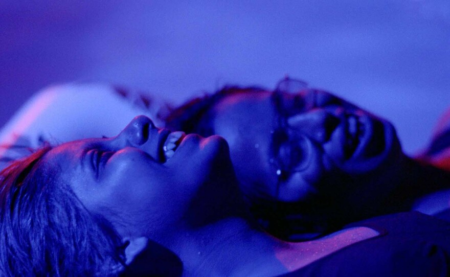 Silvia Del Carmen Castaños (left) and Estefanía “Beba” Contreras (right) lie on pool floats at night laughing together in a scene from "Hummingbirds."