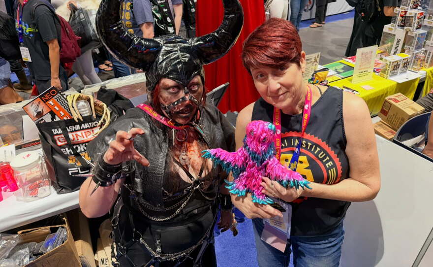Beth Accomando (right) poses with her Film Geeks booth mate, Celeste Lopez, and her latest Hedorah soft-vinyl collectible during Comic-Con on July 25, 2026.